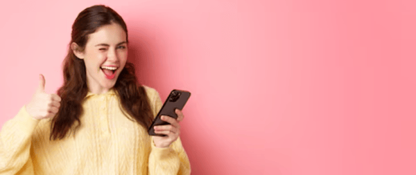 Smiling woman in a yellow sweater holding a mobile device with a thumbs up Smiling woman in a yellow sweater holding a mobile device with a thumbs up