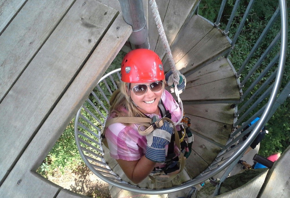 Woman smiling on a spiral staircase with zipline gear